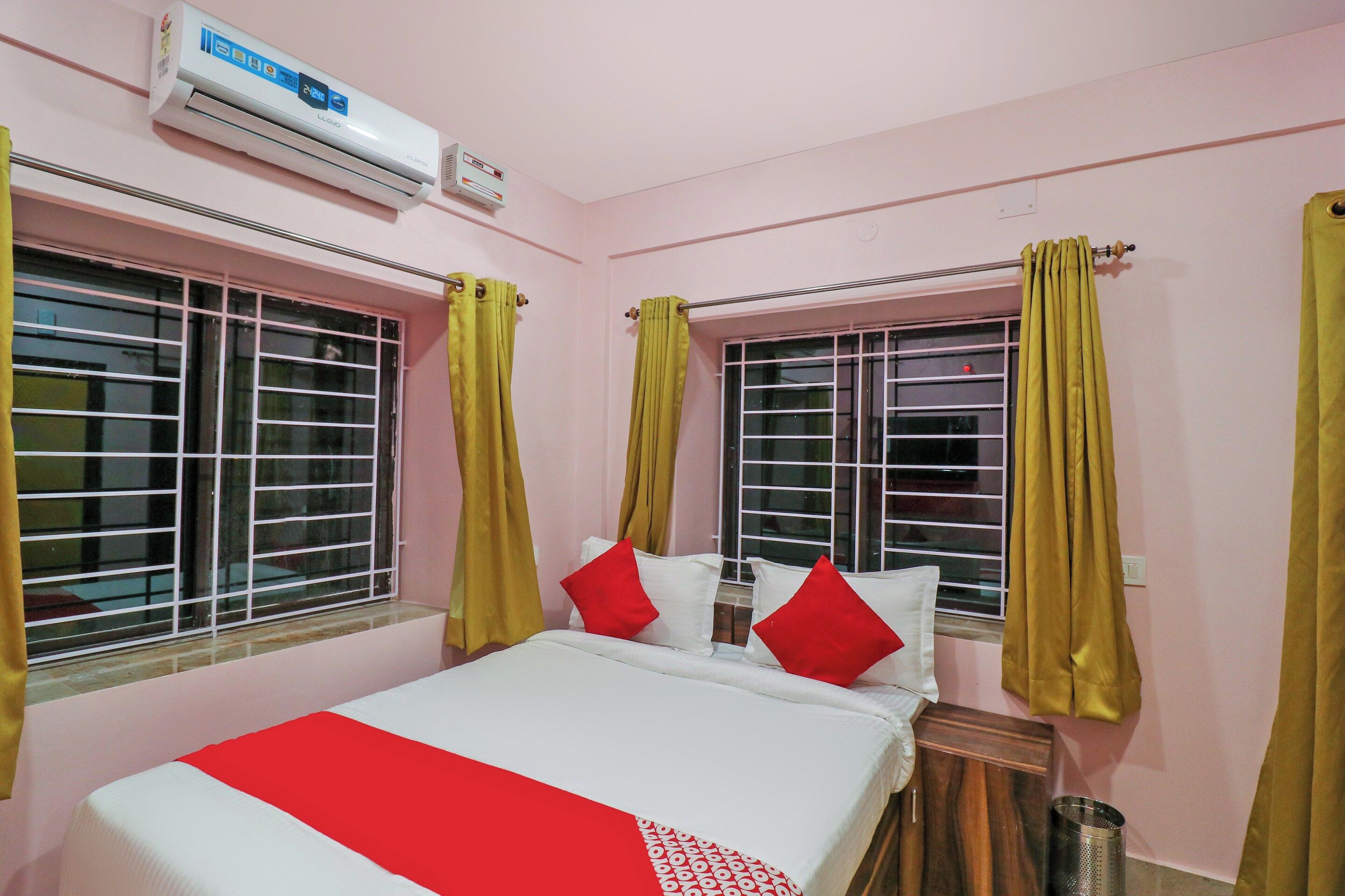 A hotel room with a bed, curtains, an air conditioning unit, and a window.