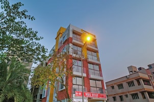 Un edificio de varios pisos con un llamativo frente rojo y amarillo, un letrero visible que dice 'NEO STAY', y un farol en primer plano.
