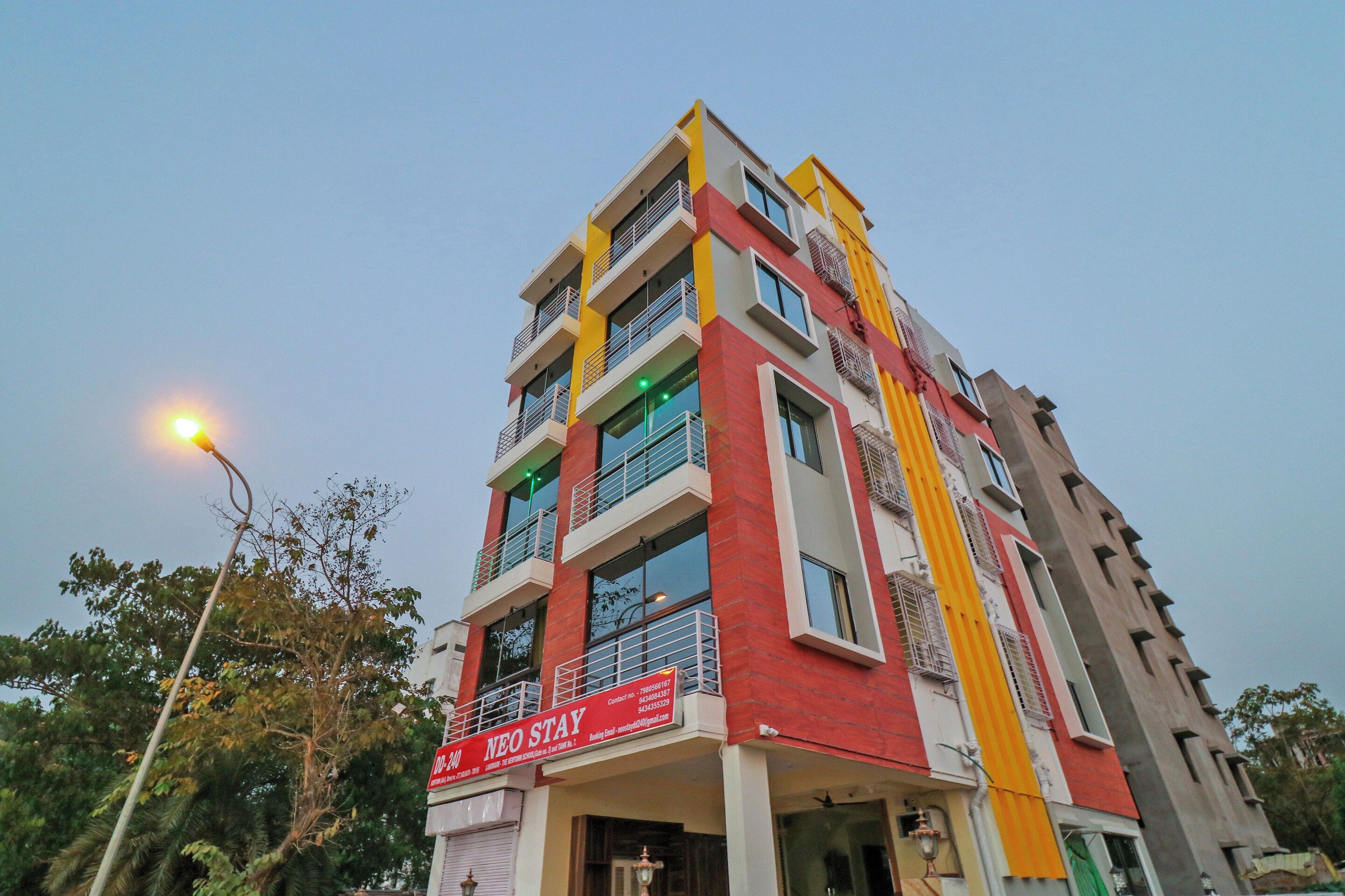Un edificio de varios pisos con fachada roja y amarilla, balcones y un letrero que dice 'NEO STAY'.