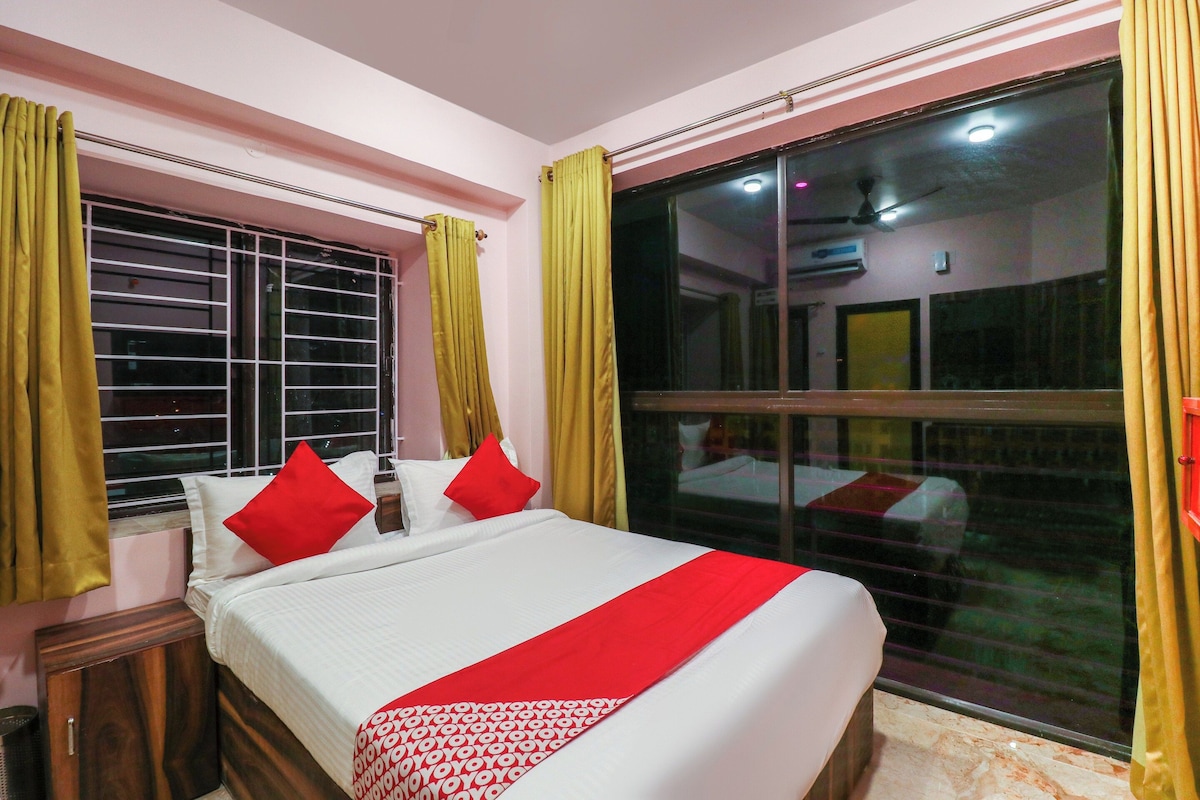 A hotel room with a bed, a window with curtains, and a view of the outside.