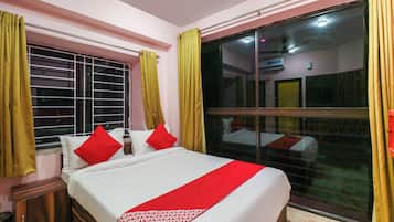 A hotel room with a bed, a window with curtains, and a view of the outside.