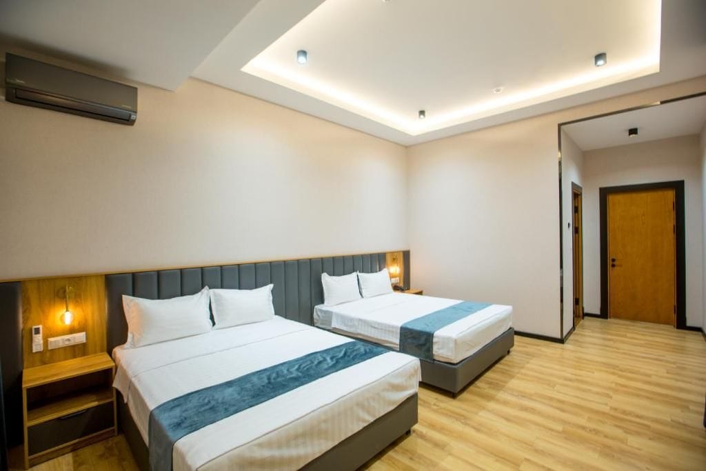 Habitación de hotel con dos camas, piso de madera y lámpara en el techo.
