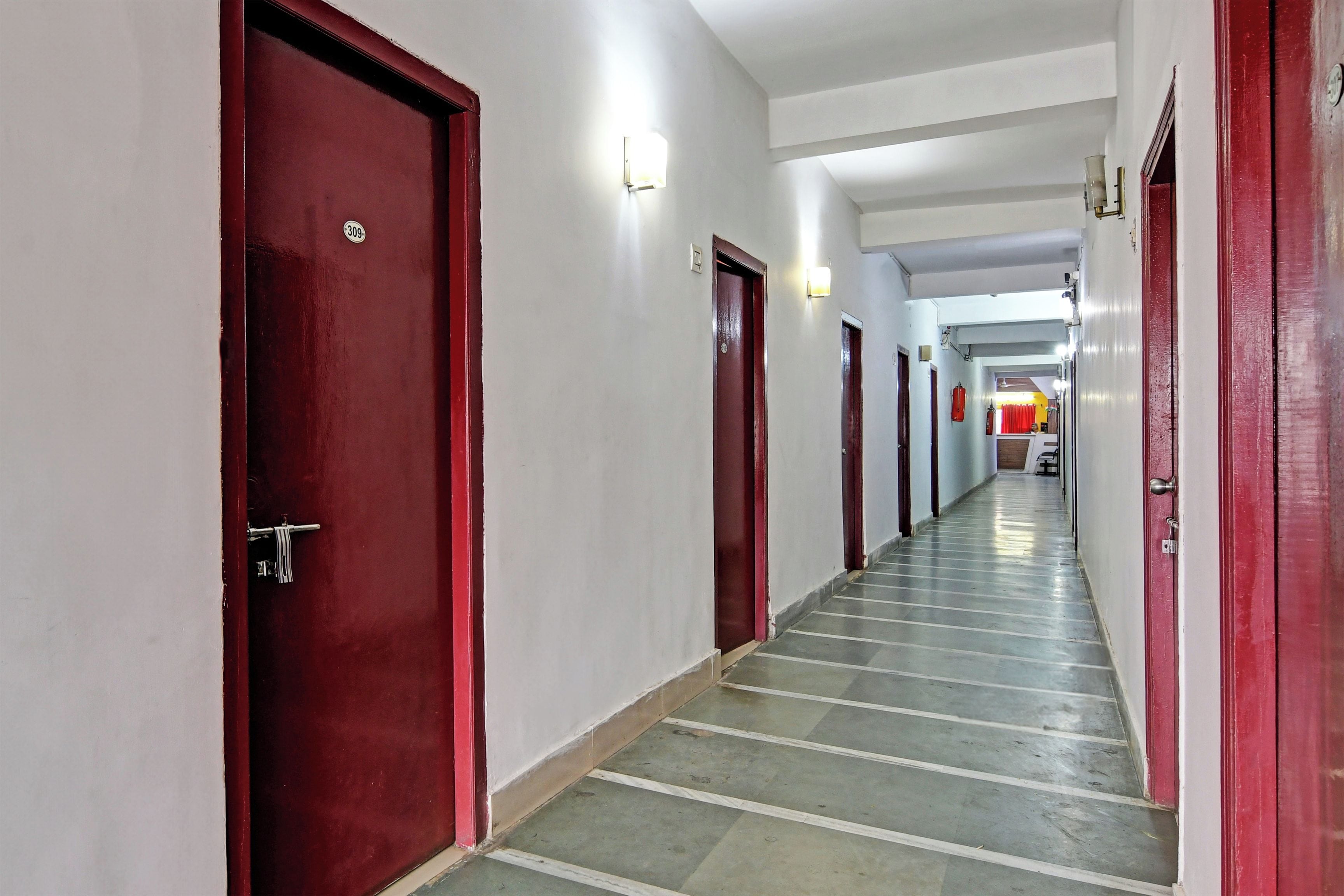 Un pasillo con puertas rojas y paredes blancas que conduce a una habitación con una cama y un ventanal.