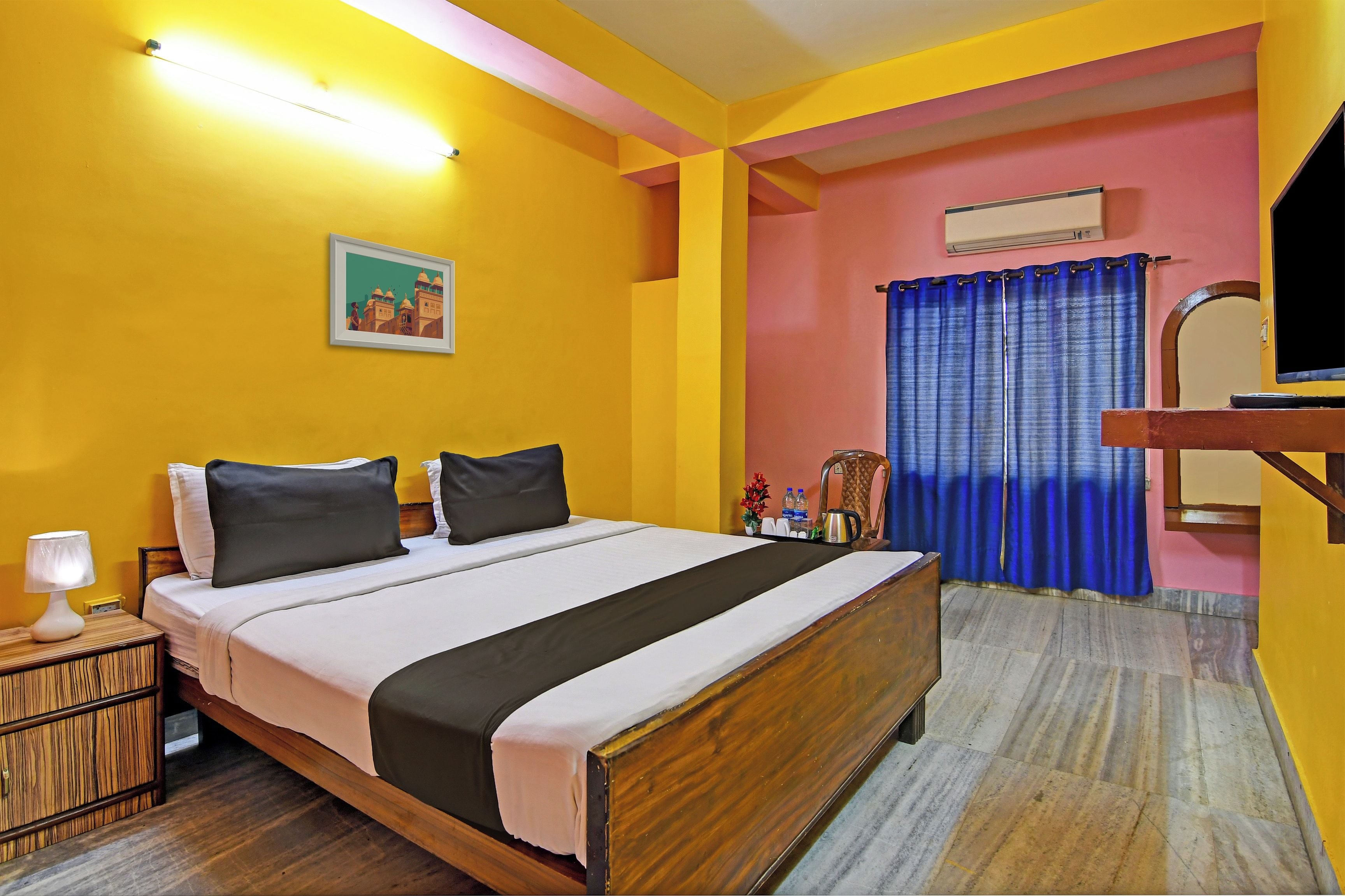 A hotel room with a bed, bedside table, lamp, and a painting on the wall.