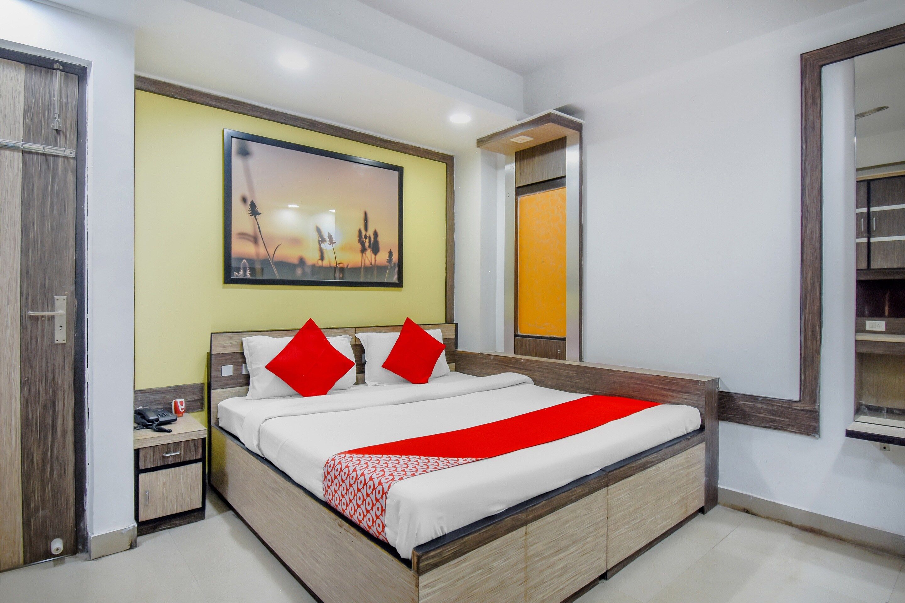 A hotel room with a bed, a nightstand, a bedside table, a mirror, and a painting on the wall.