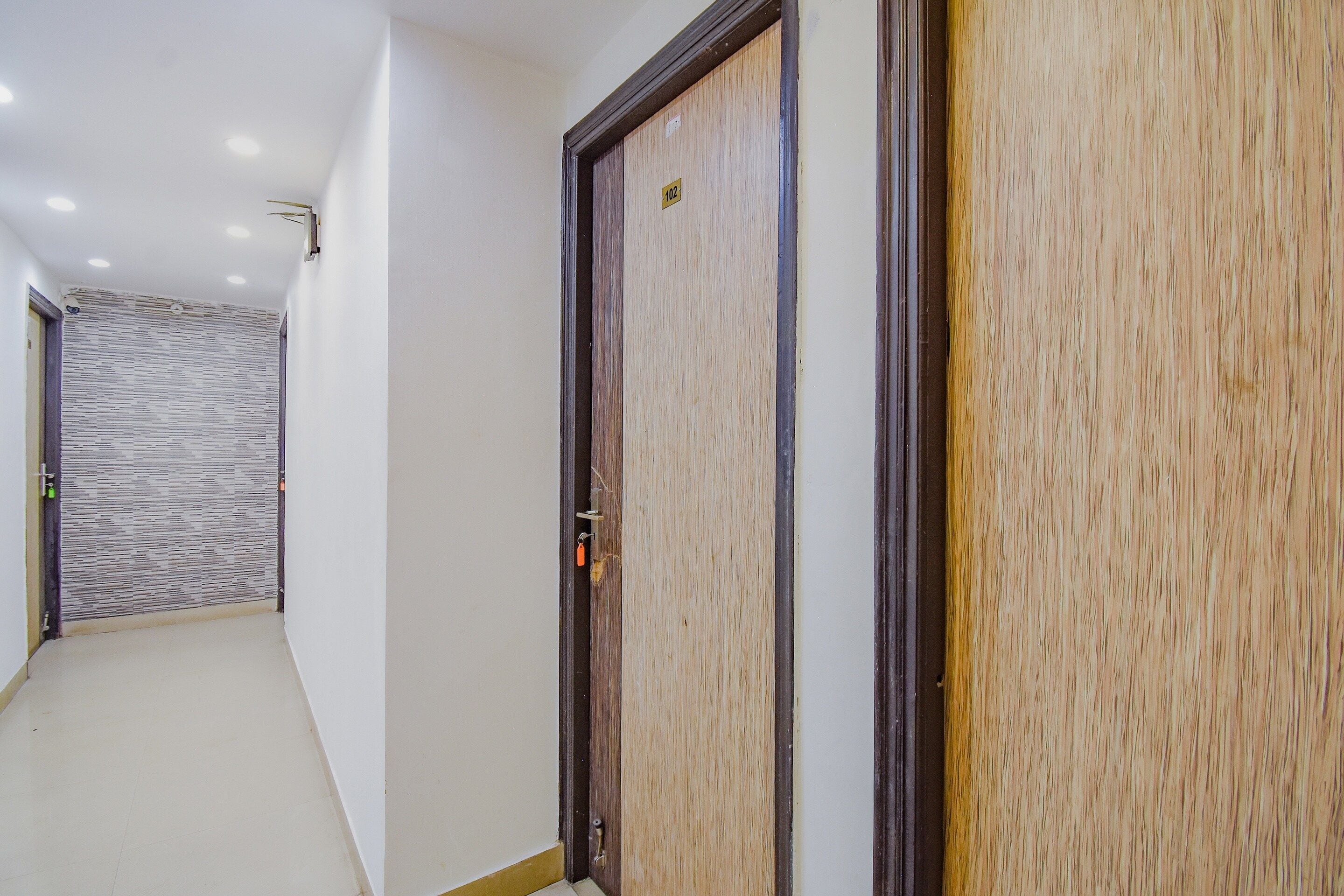 A hallway with a wooden door on the right, a textured wall on the left, and a tiled floor.