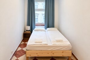 A narrow room with a bed, a nightstand, and a window with curtains. - Vienna Beyond Your Door 1BR and Private Lounge (Vienna)