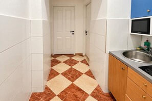 A narrow kitchen with white tiled walls, a checkered floor, and a door leading to another room. - Vienna Beyond Your Door 1BR and Private Lounge (Vienna)