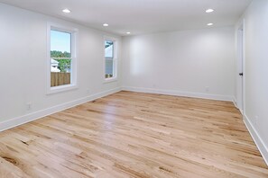 Une pièce avec un plancher en bois, des murs blancs et deux fenêtres.