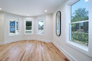 Una habitación con ventanas amplias, piso de madera y un espejo fijado a la pared.