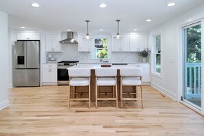 A modern kitchen with white cabinetry, a stainless steel refrigerator, a gas stove, and a wooden island with bar stools. - Fairfield -Charming Completely Renovated 3-bedroom house with AC & 2 car garage. (Fairfield)