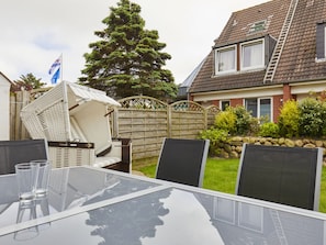 A glass-top table with chairs, a wooden fence, and a house with a sloped roof. - New Love - Suderstr. 18c (Sylt)