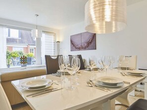 A dining area with a long table set for a meal, a modern pendant light, and a view of the outside. - New Love - Suderstr. 18c (Sylt)