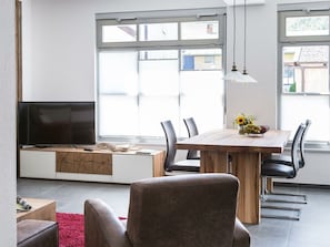 A modern living room with a TV, seating area, dining table, and large windows. - Holiday Apartment With 2 Bedrooms (Mittenwald)