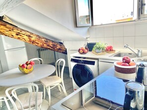 Eine kleine Küche mit Essbereich, einer Waschmaschine und einem Fenster mit Blick auf ein Gebäude.