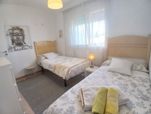 A hotel room with two beds, a bedside table with a lamp, a window with curtains, and a wall-mounted painting. - New Listing (Ronda)
