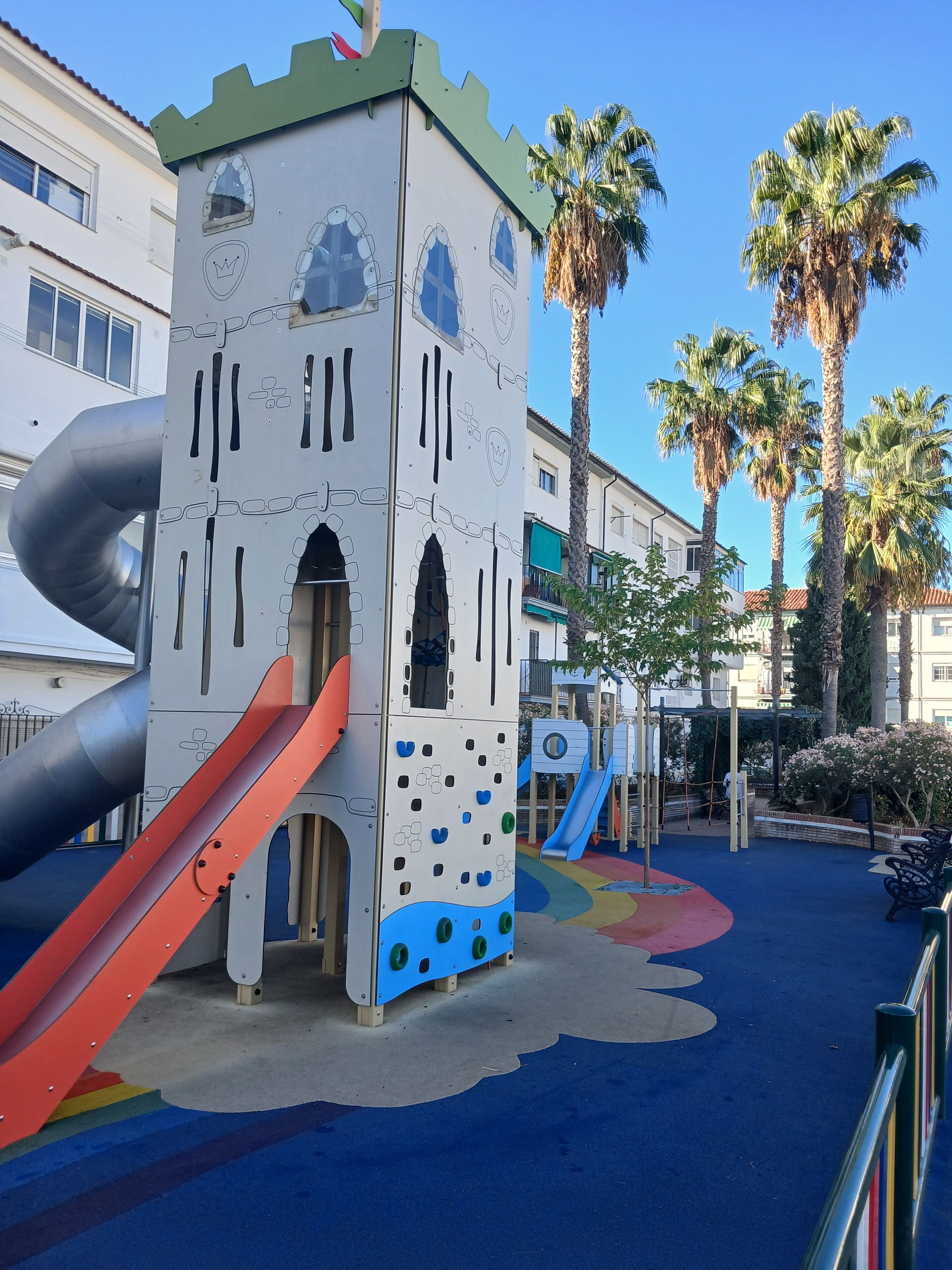Une aire de jeux avec un toboggan, un mur d’escalade et une structure ressemblant à un château.