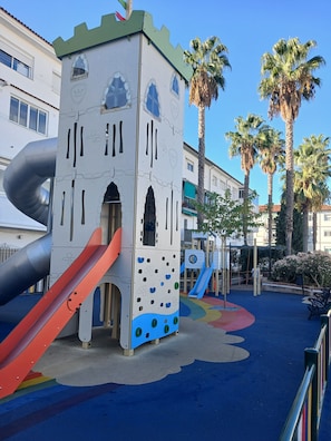 Une aire de jeux avec un toboggan, un mur d’escalade et une structure ressemblant à un château.