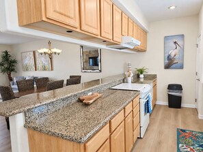 A kitchen with granite countertops, wooden cabinets, a built-in oven, and a trash can. - Las Flores #B Spacious 2/2 W/Easy Beach Access (South Padre Island)