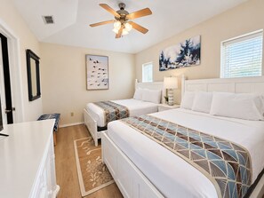 A hotel room with two beds, a ceiling fan, a painting of birds, a window with blinds, and a door. - Las Flores #B Spacious 2/2 W/Easy Beach Access (South Padre Island)