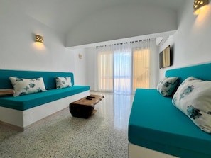 Ein modernes Wohnzimmer mit türkisfarbenen Sofas, einem Holztisch und Blick durch ein großes Fenster.