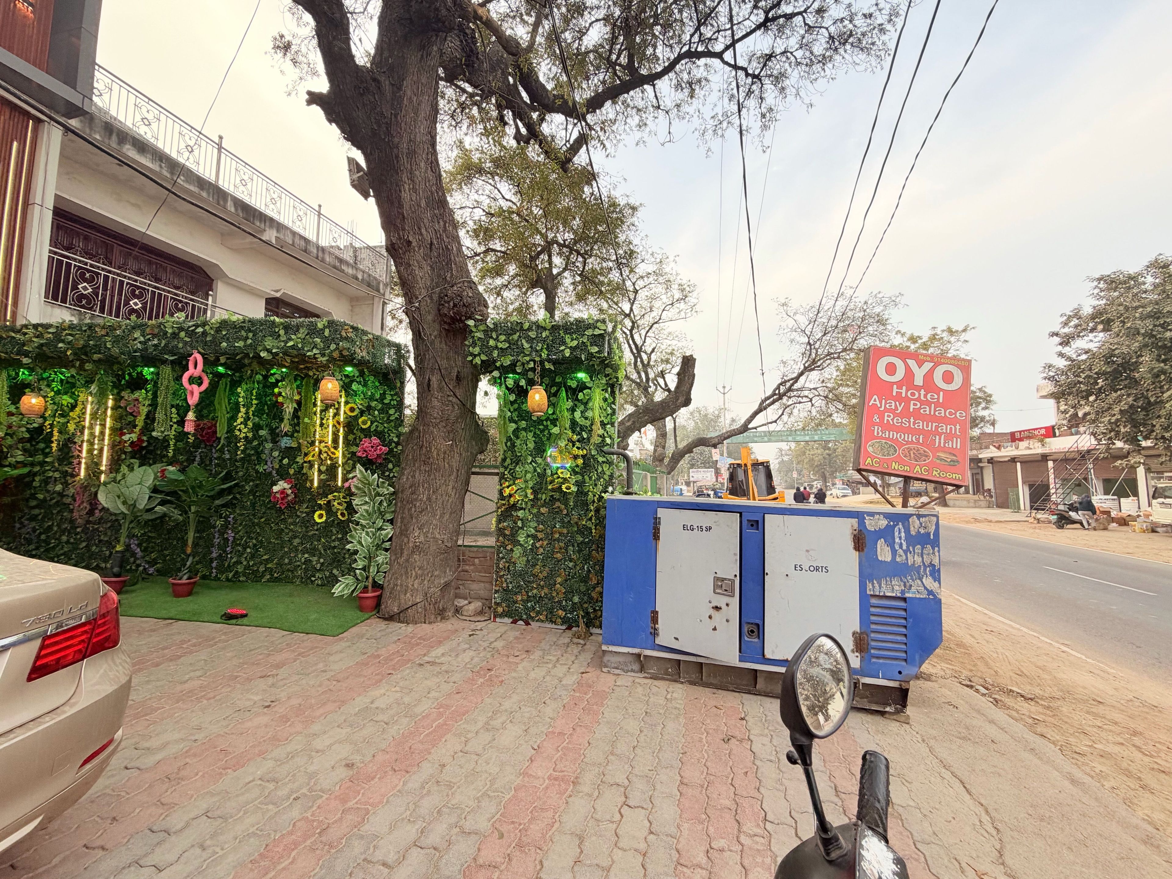 Un hotel con una pared verde decorada con plantas y luces colgantes, un coche estacionado y un cartel que indica OYO Hotel & Jay Palace Restaurant.