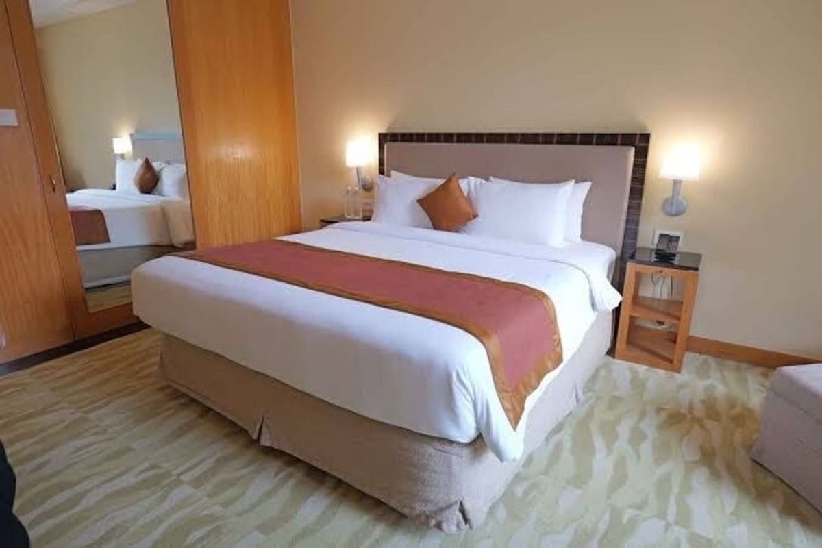 A hotel room with a large bed, a bedside table, a nightstand, a mirror, and a carpeted floor.