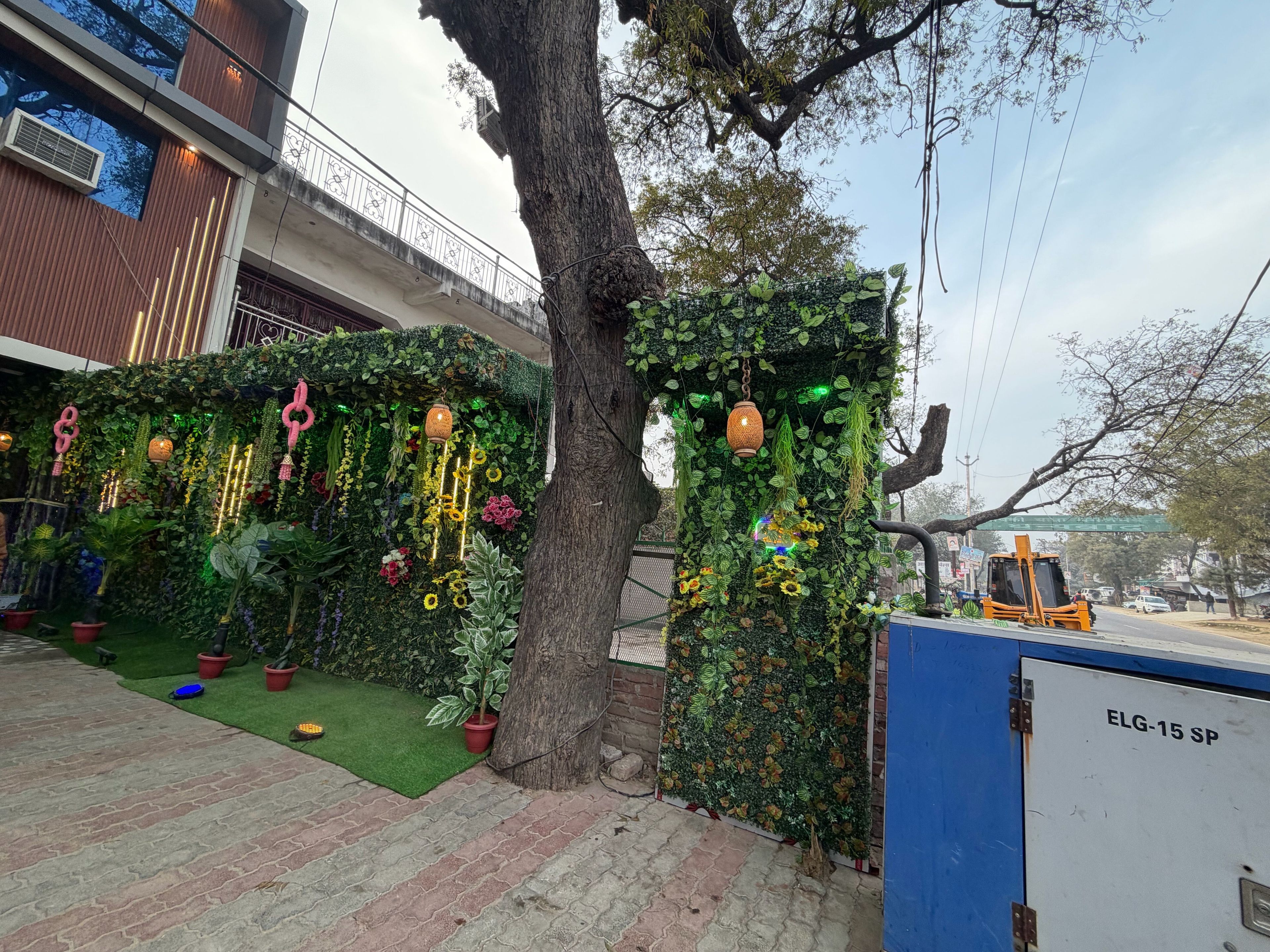 A tree-lined pathway with a decorative wall featuring plants and hanging ornaments.