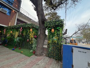 A tree-lined pathway with a decorative wall featuring plants and hanging ornaments. - HOTEL O AJAY PALACE (Lalganj)