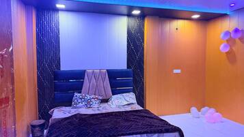 A bedroom with a bed, pillows, a blanket, and a wall with a patterned curtain.