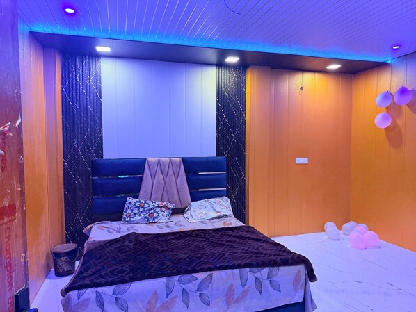 A bedroom with a bed, pillows, a blanket, and a wall with a patterned curtain.