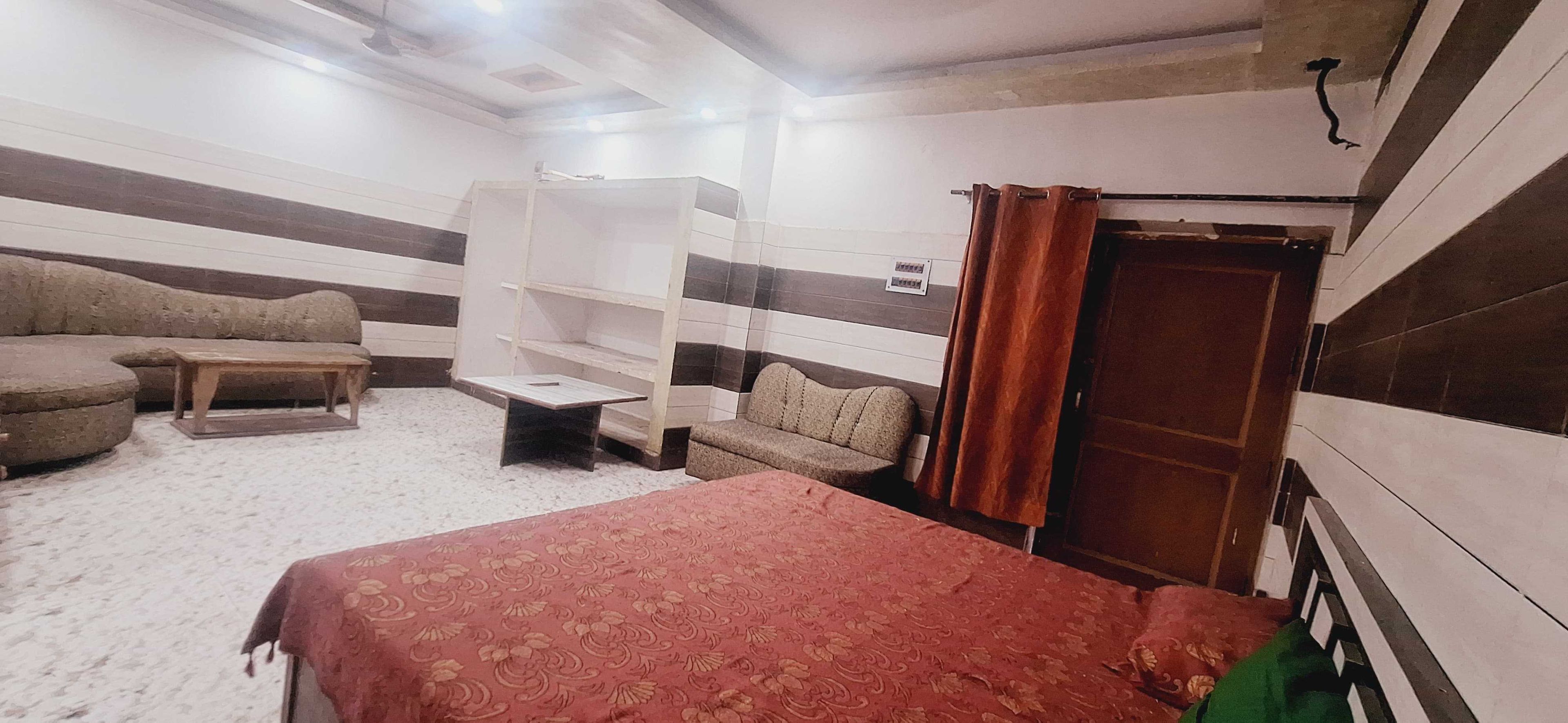 A room with a bed, a sofa, a small table, and a built-in shelf unit.