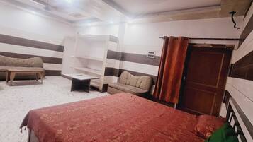 A room with a bed, a sofa, a small table, and a built-in shelf unit.