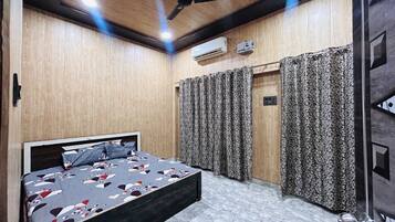A bedroom with a bed, curtains, an air conditioning unit, and a ceiling fan.