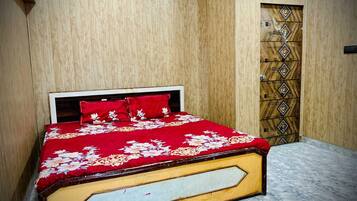 A bed with a floral bedspread and red pillows in a room with wooden panel walls and a marble floor.