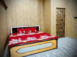 Una cama con colcha floral y almohadas rojas en una habitación con paneles de madera y suelo de mármol.