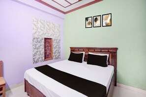 Un dormitorio con cama, cabecero de madera, ventana con marco decorativo y tres cuadros colgados en la pared.