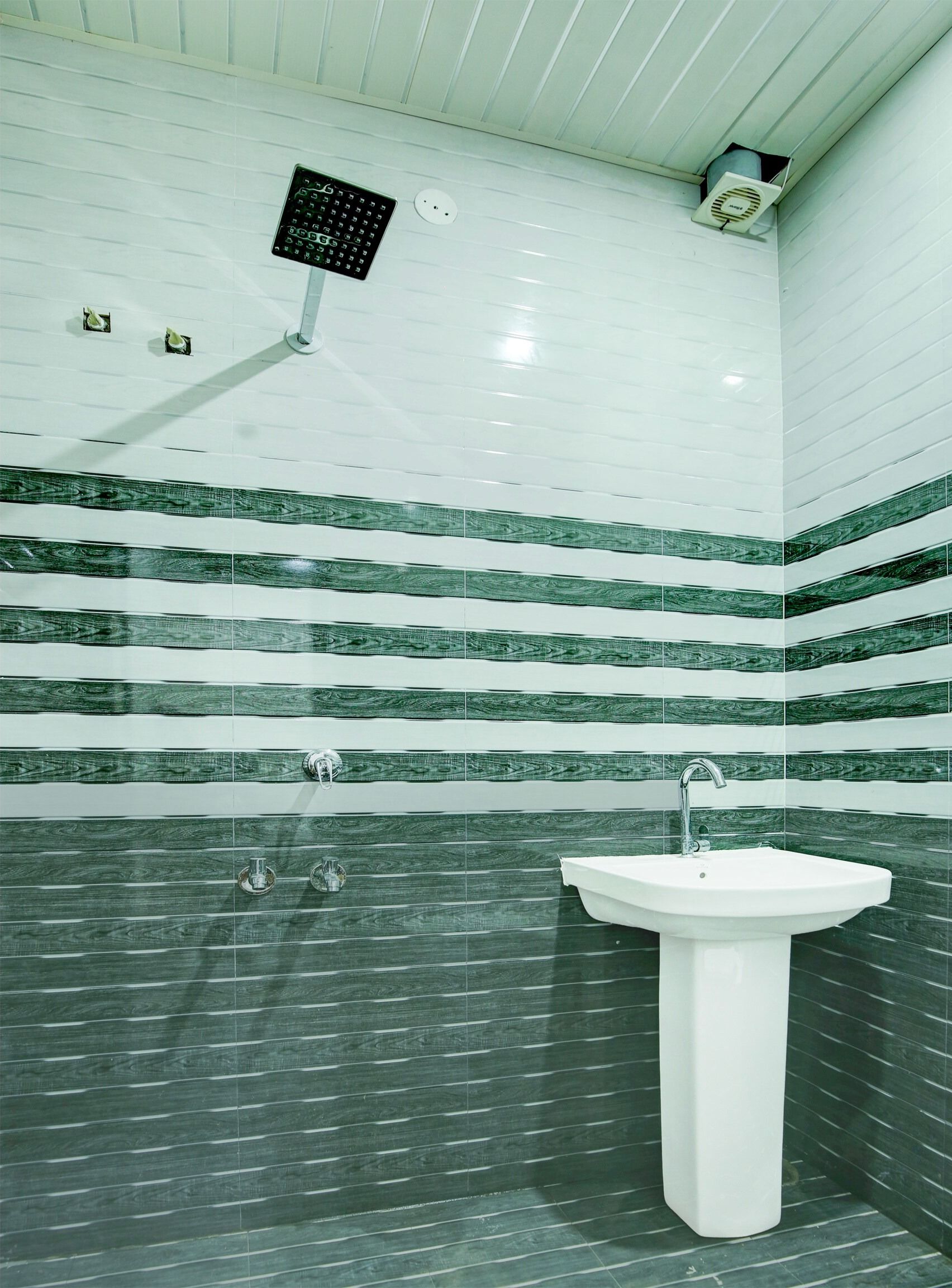 A bathroom with a white sink, a shower head, and a tiled wall with a wood grain pattern.