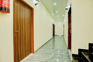 A corridor with wooden doors, marble flooring, and wall-mounted light fixtures.