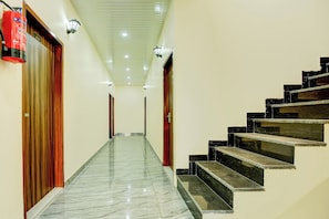 A hallway with a marble floor leading to a staircase with black steps. - Hotel O by OYO R.K STAY (Ludhiana)