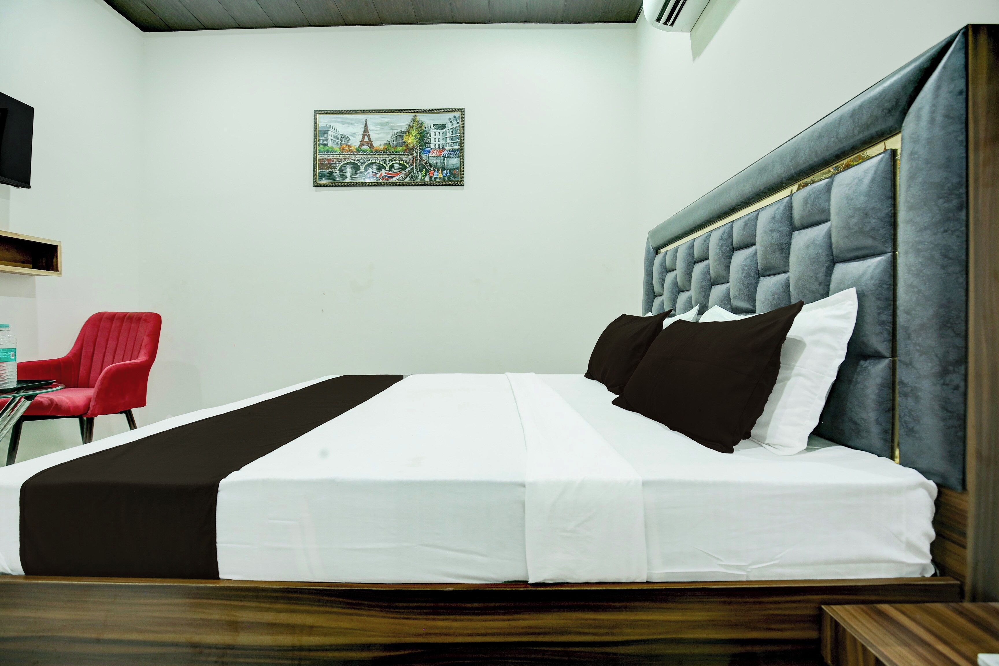 A hotel room with a bed, a red chair, a small table, and a picture on the wall.