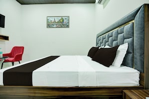 Une chambre d’hôtel avec un lit, une chaise rouge, une petite table et un tableau accroché au mur.