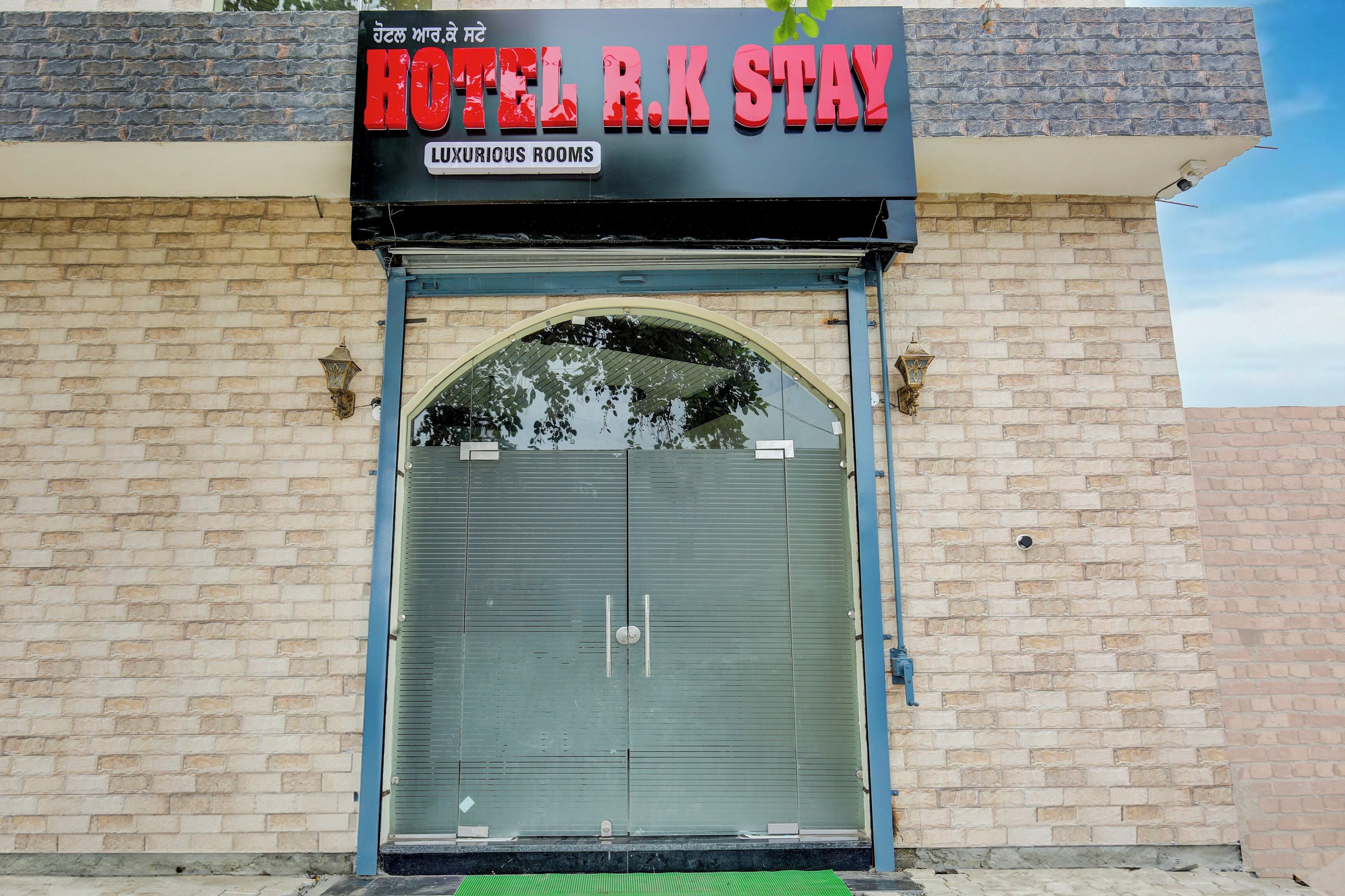 Un hotel con un letrero que dice 'HOTEL R.K STAY' y 'HABITACIONES LUSOSAS' sobre una puerta con contraventana cerrada.