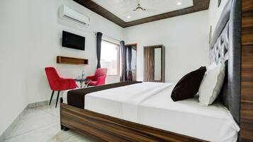 A hotel room with a bed, a TV, a desk with a chair, and a window with curtains.