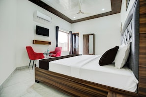 Une chambre d’hôtel avec un lit, une télévision, un bureau avec une chaise et une fenêtre avec des rideaux.