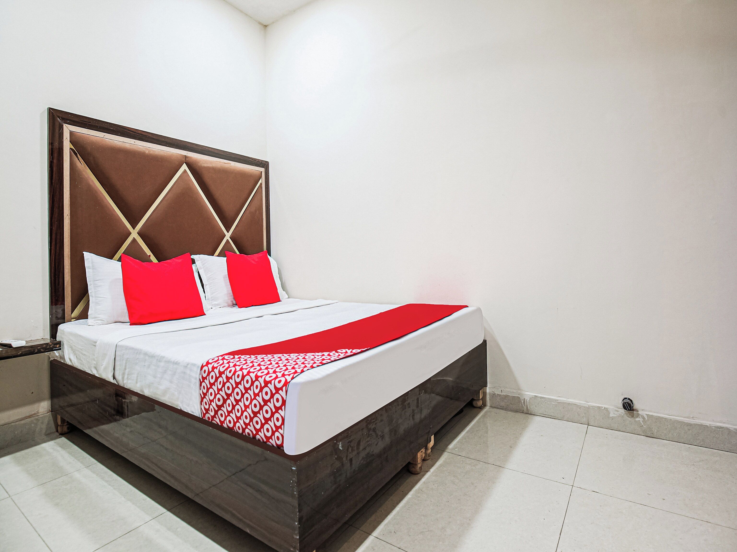 Una cama con cabecera, ropa de cama blanca y detalles en rojo.