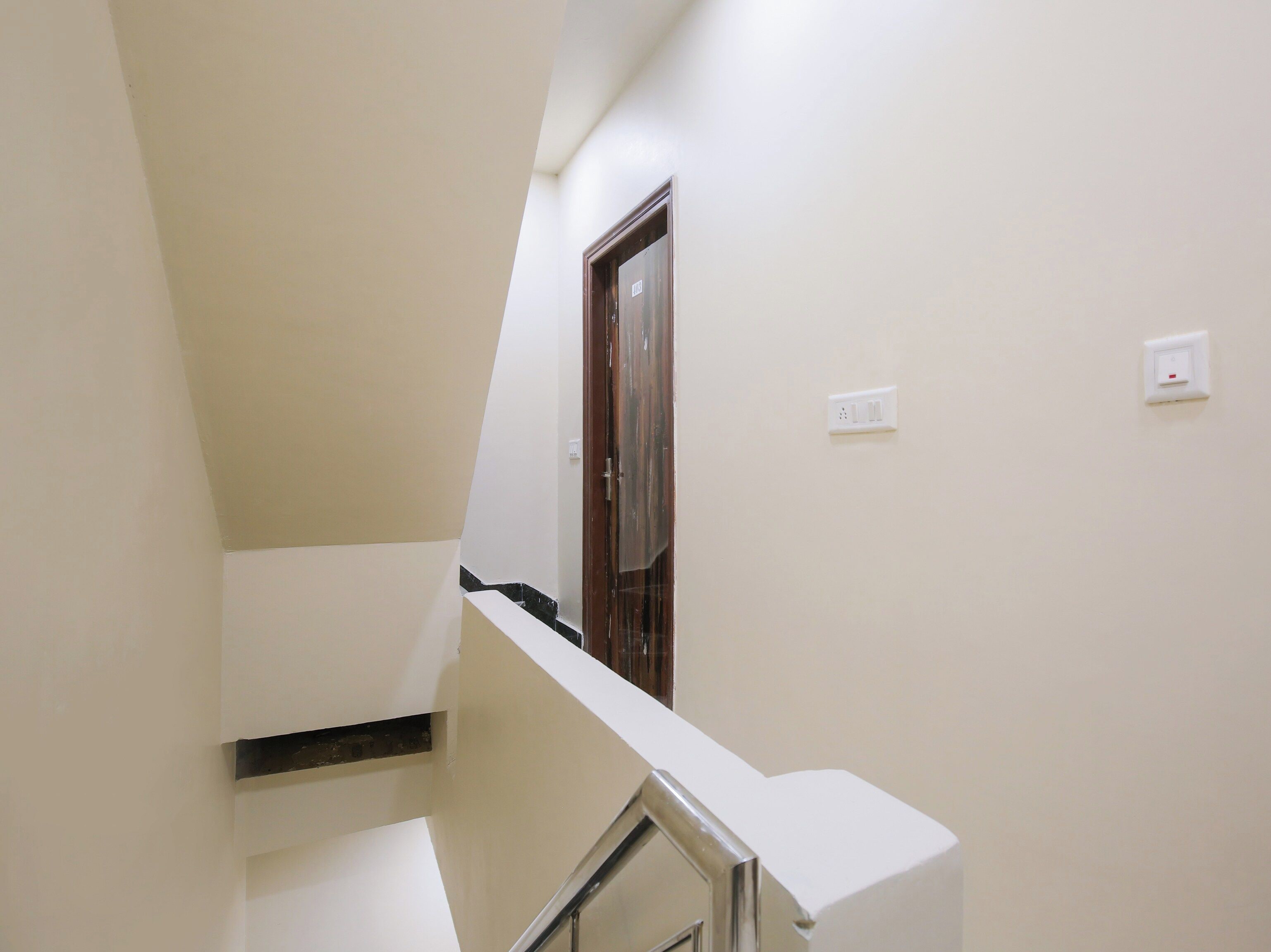 Un escalier étroit avec une main courante, une porte en bois et un interrupteur sur le mur.