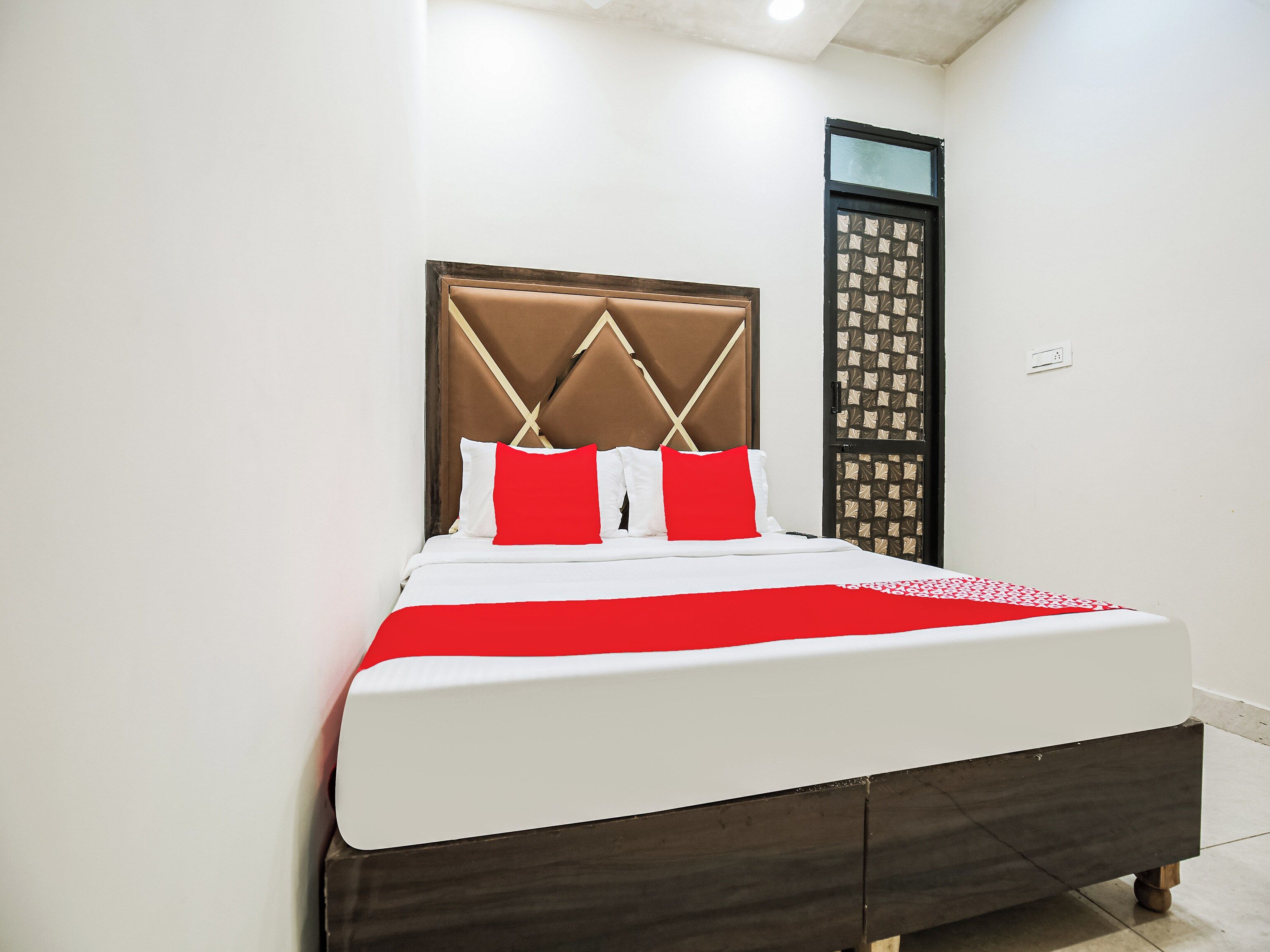 A bed with a headboard, white bedding, and a red accent pillow.