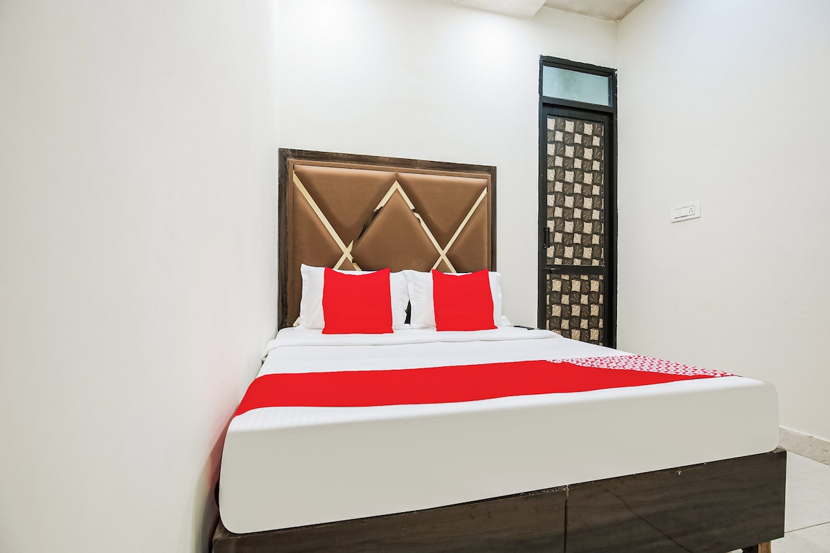 A bed with a headboard, white bedding, and a red accent pillow.