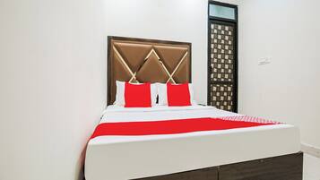 A bed with a headboard, white bedding, and a red accent pillow.